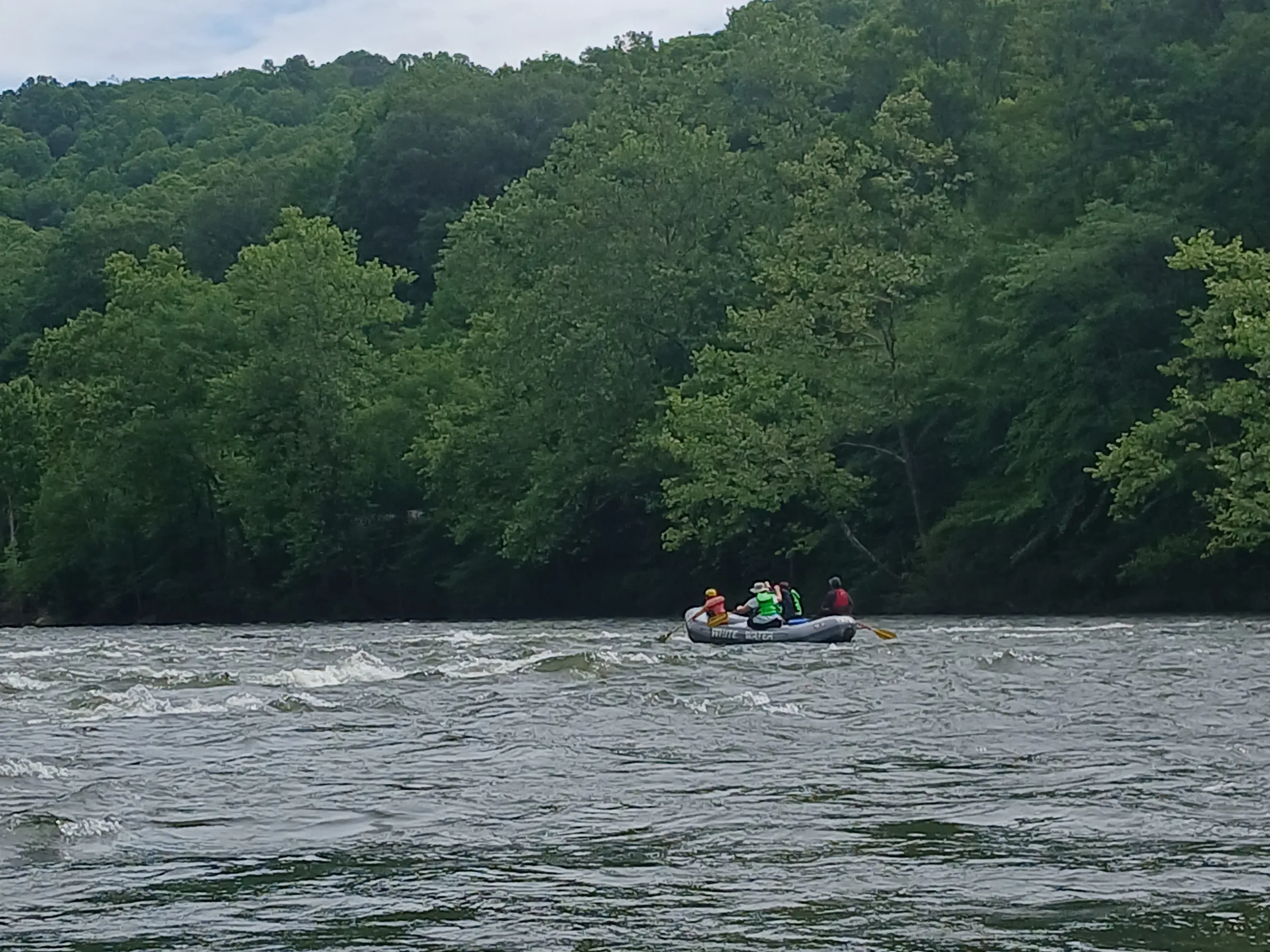 Group rafting on a river surrounded by lush green trees under a cloudy sky.