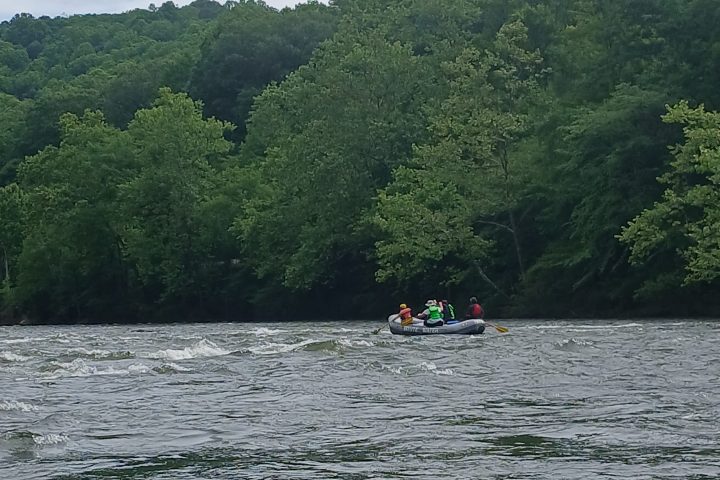 Group rafting on a river surrounded by lush green trees under a cloudy sky.