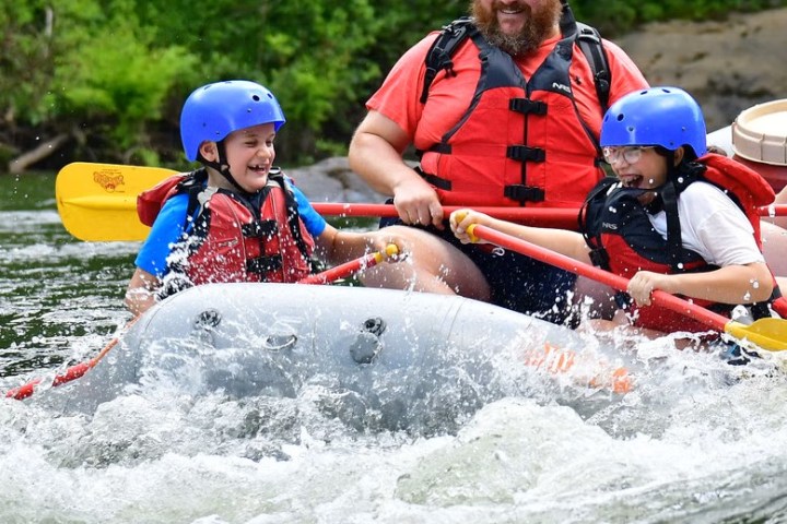 Three people in safety gear enjoying a rafting adventure on a river, surrounded by splashing water.