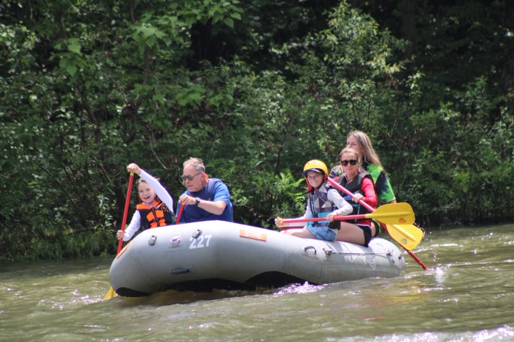 Four people rafting on a river in an inflatable boat, surrounded by trees.