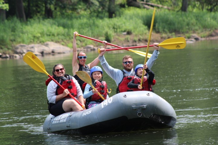 Group of people in life jackets smiling and holding paddles on a raft in a river.