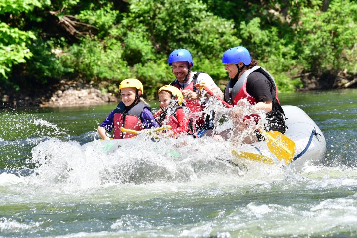 Group of people in helmets and vests rafting on a river.
