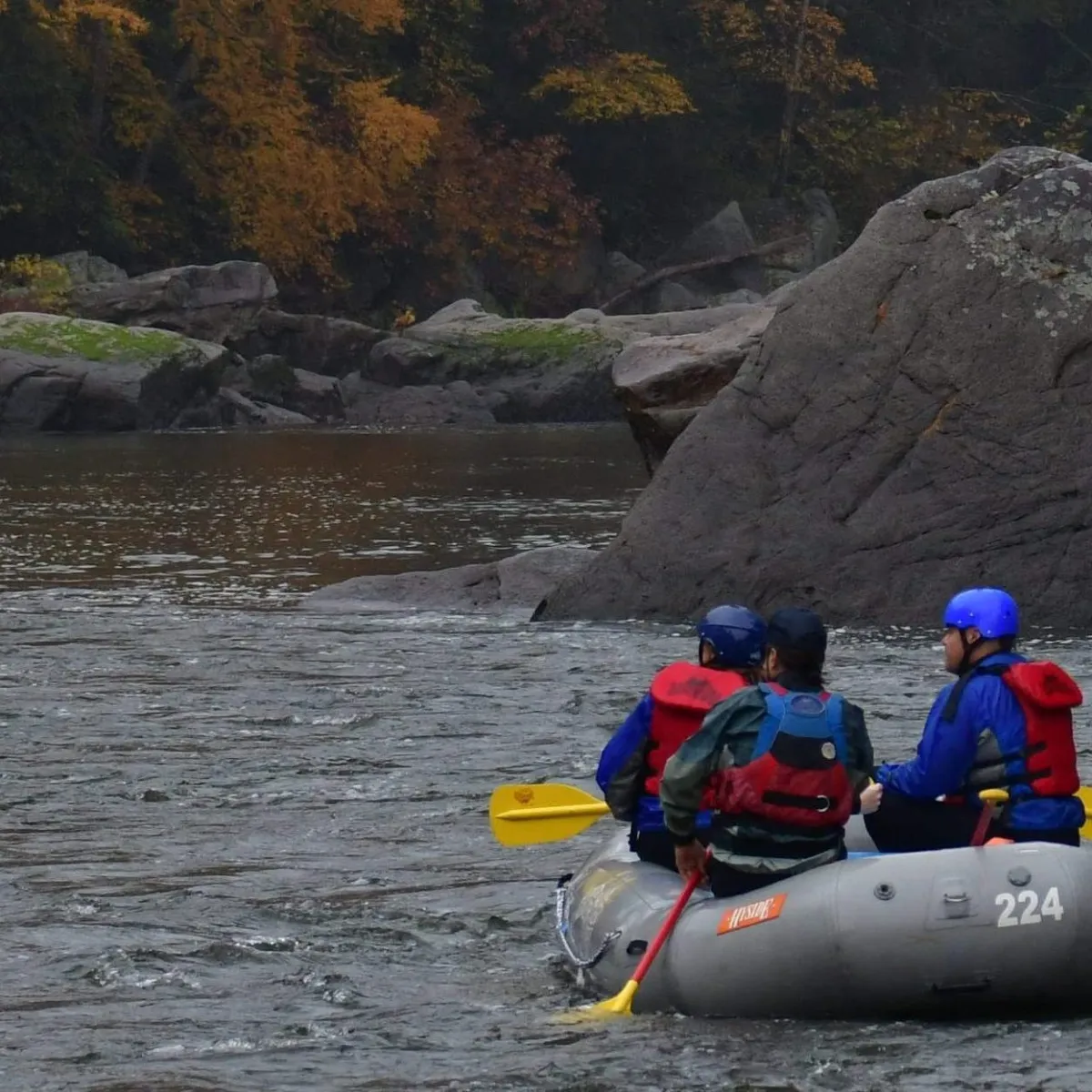 Two people rafting down a river surrounded by autumn trees and rocks.