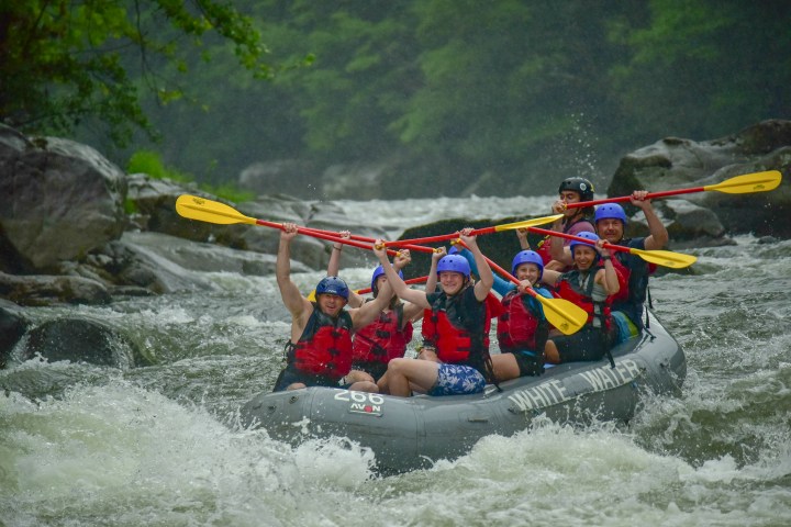 Group of people white water rafting, raising paddles in excitement.