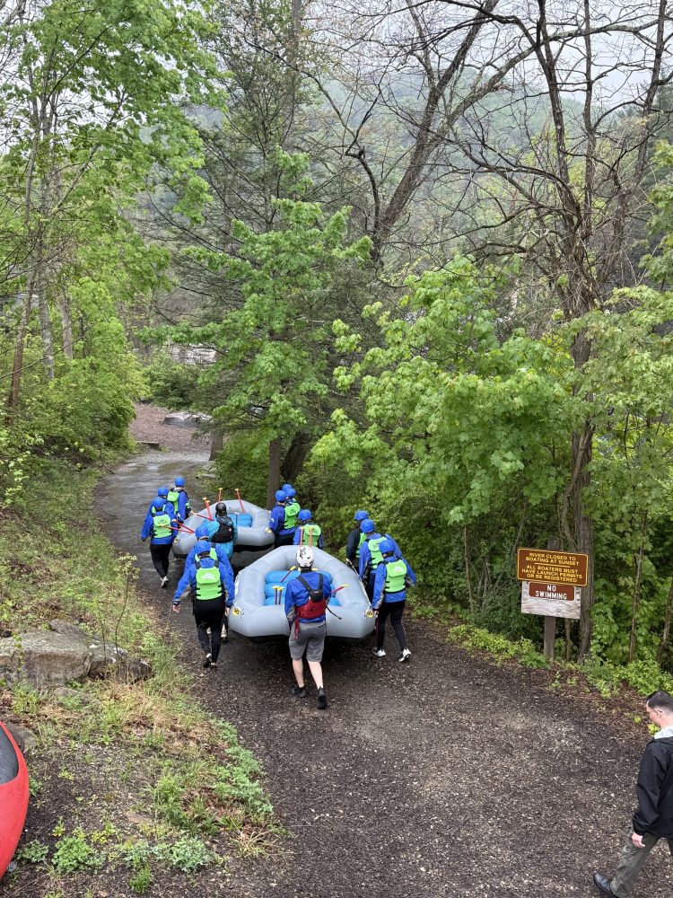 Group carrying rafts down a forest path towards a river.