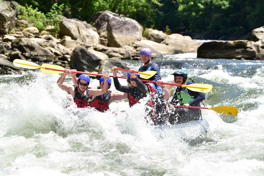 Group of people whitewater rafting through rapids, wearing helmets and life vests.