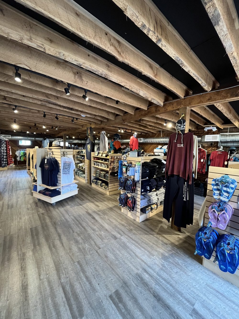 Clothing store interior with wooden beams and various apparel displays.