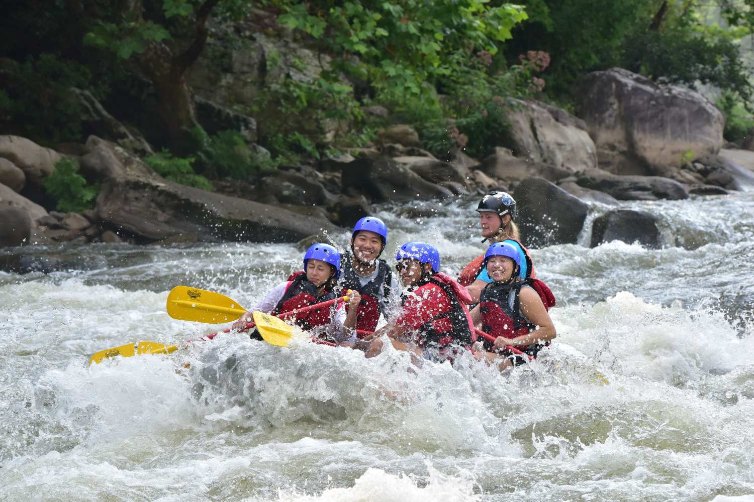 Group of people white-water rafting on a river, wearing helmets and life jackets.